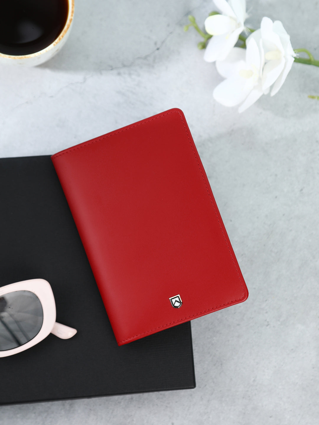 Multi purpose ruby red leather passport case on a black surface with sunglasses and white flowers in the background #color_ruby red